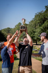 Group celebrates winning the Louisiana Christian University Tricycle Race, holding up the champion trophy.