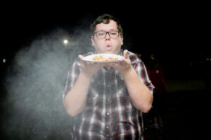 Man in glasses blowing powdered sugar off a