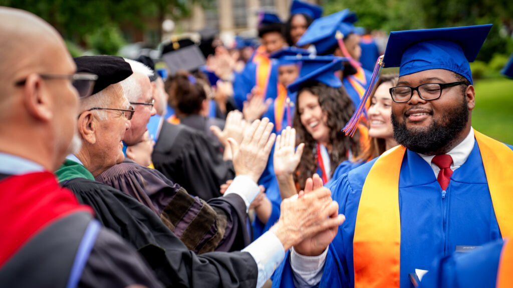 Members of the Class of 2026 walking through the Arch at the front of campus being congratulated by faculty and staff for their accomplishments.